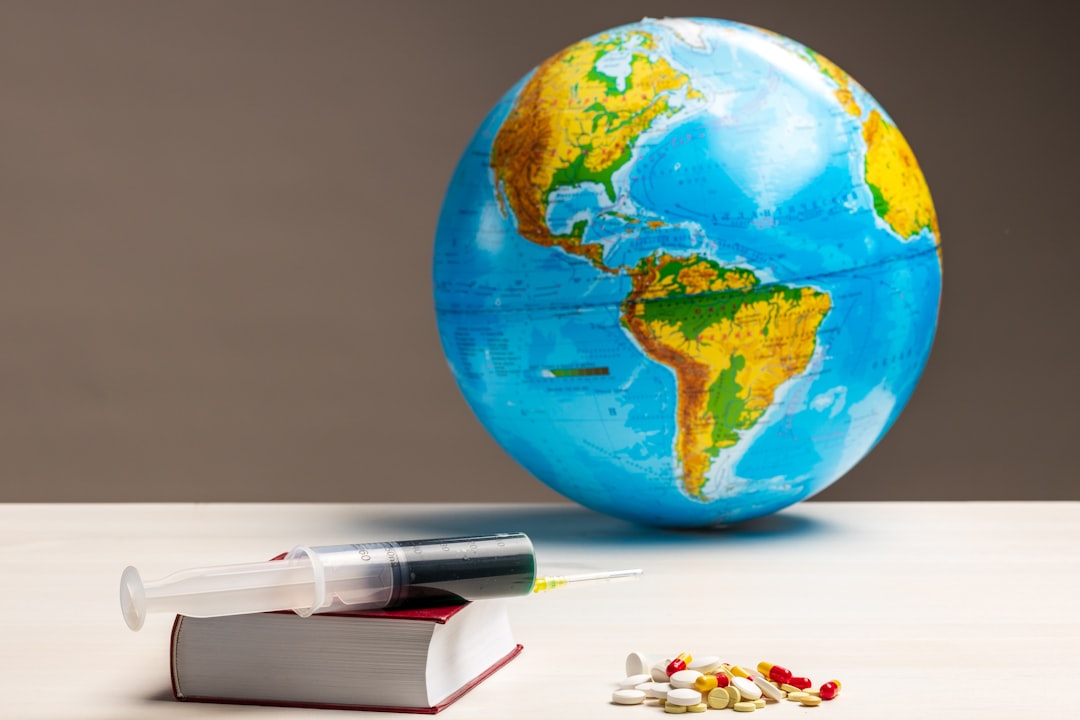 A globe representing the world next to a syringe and assorted pills on a stack of books